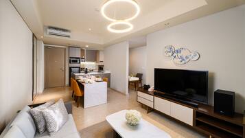 A modern living room with a sofa, coffee table, TV, and a dining area in the background.