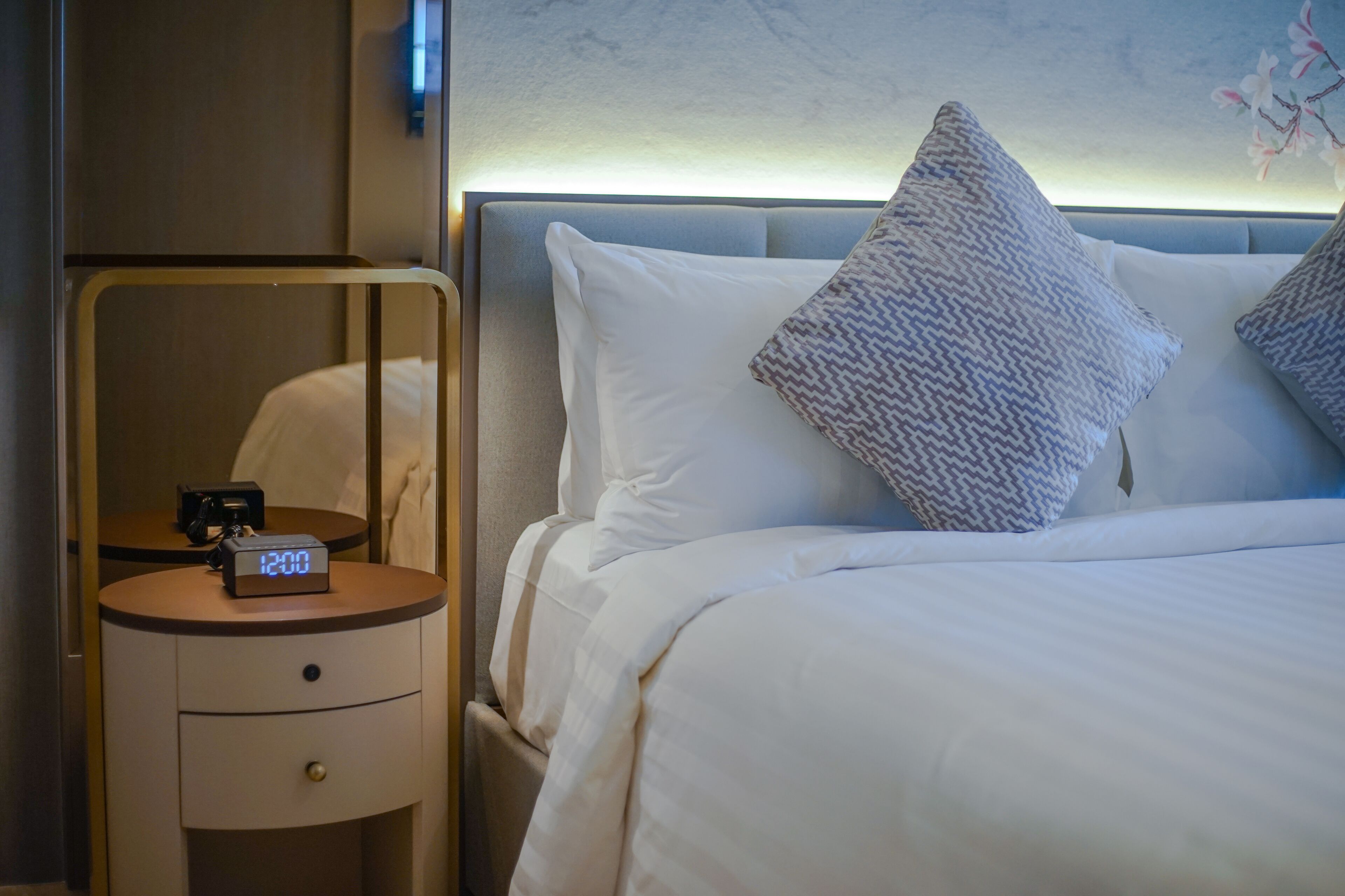 A hotel room with a bed, a bedside table with a digital clock, and a nightstand.