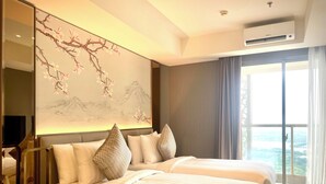 Quarto de hotel com duas camas, uma janela grande com vista, ar condicionado fixado na parede e mesa de cabeceira com relógio.