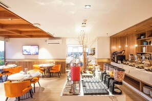 Ein moderner Essbereich mit orangefarbenen Stühlen, einem Buffet mit verschiedenen Speisen und einem an der Wand befestigten Fernseher.