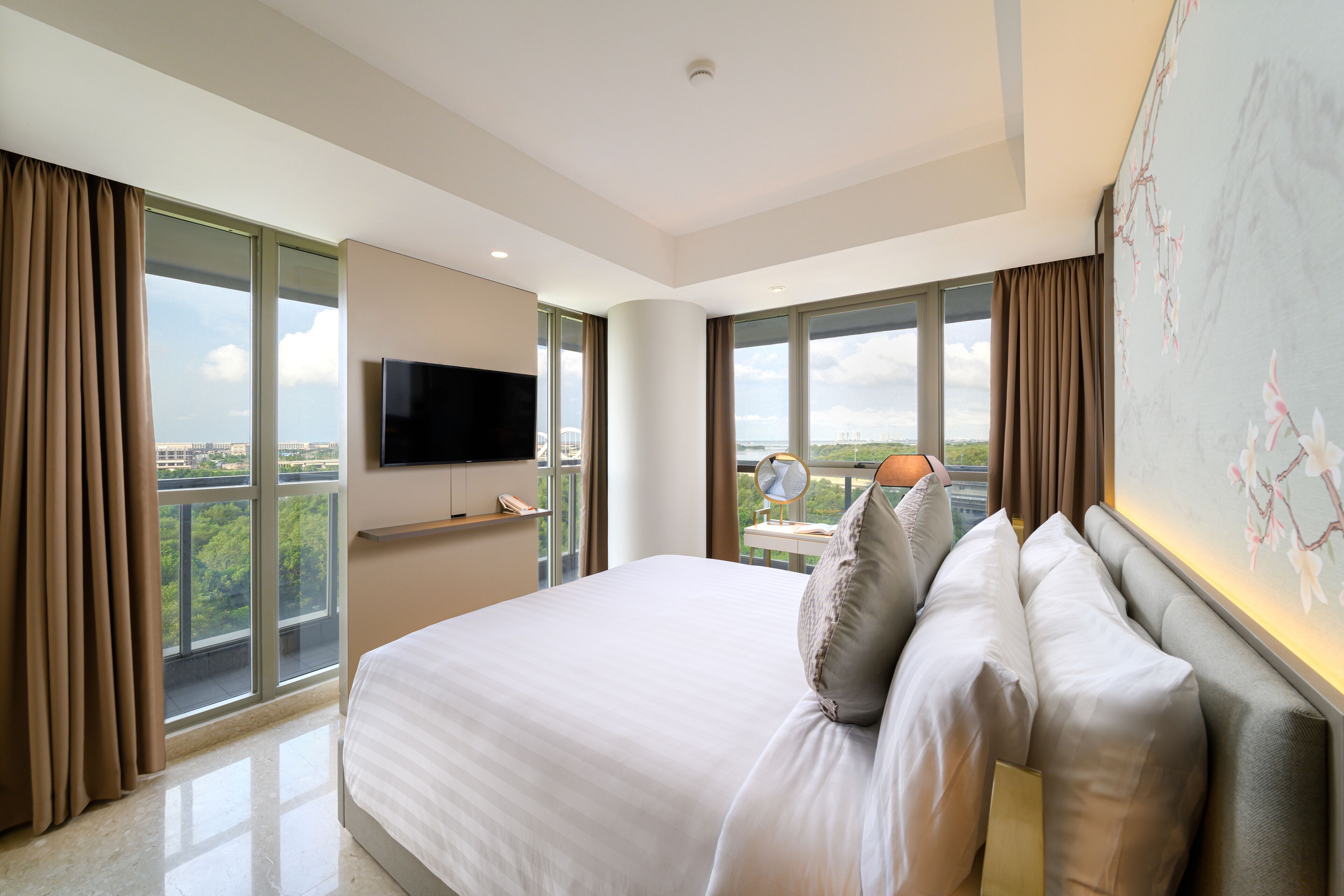 Una camera d'albergo moderna con un letto grande, una TV a schermo piatto, un balcone con vista sulla città e un'ampia finestra con tende.