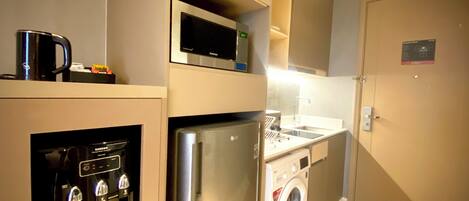 Eine kleine Küche mit Mikrowelle, Kühlschrank, Backofen und Waschmaschine.