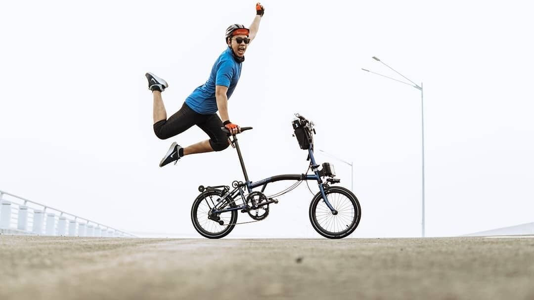 Une personne réalisant une figure de cascade à vélo sur une surface en béton, avec un pont en arrière-plan.