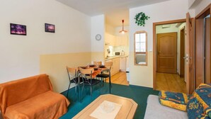 Un espacio habitable compacto con comedor, kitchenette y un pequeño pasillo que lleva a una puerta.