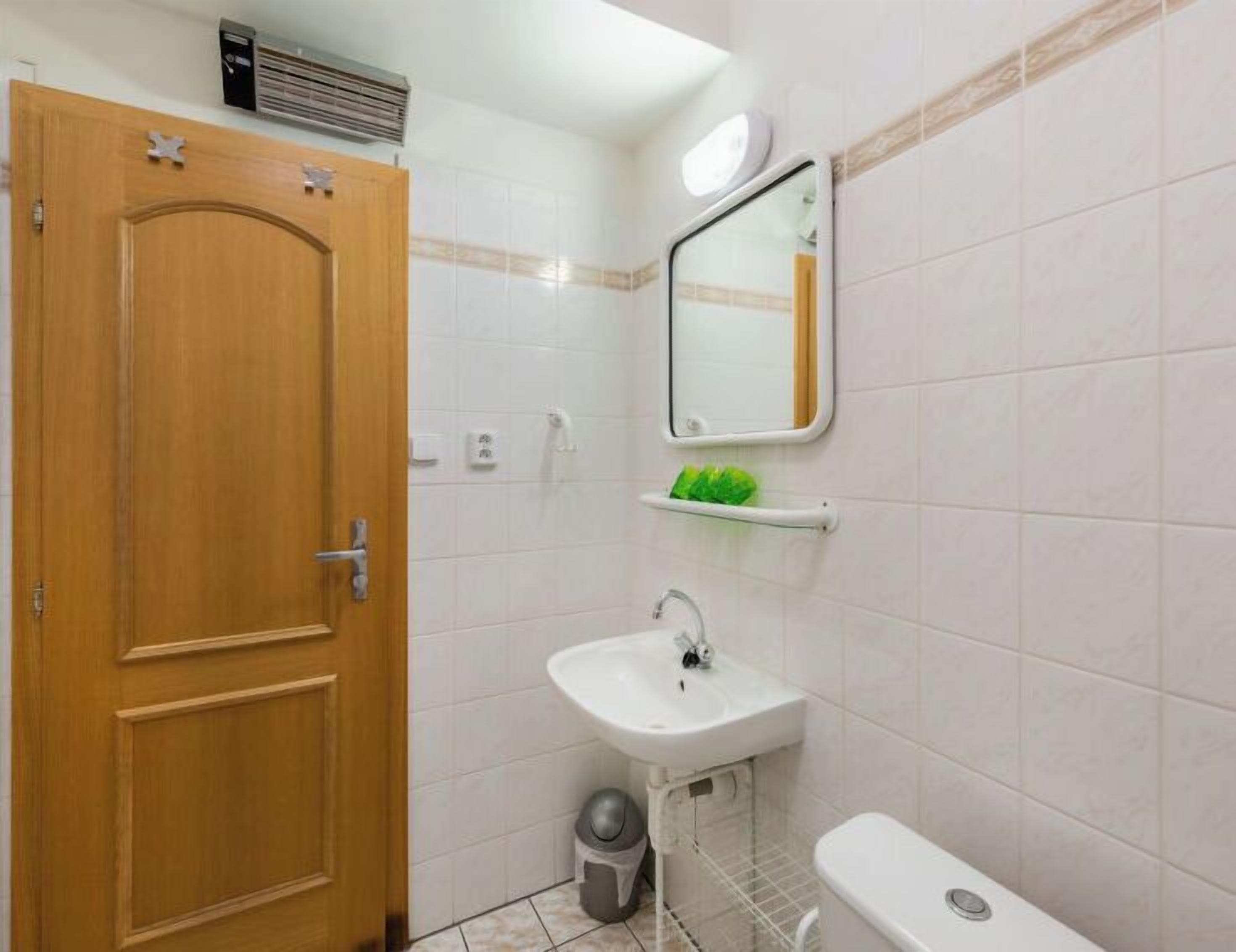 A bathroom with a wooden door, a white sink, a mirror, and a toilet.