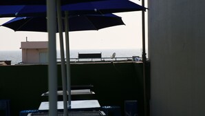 A balcony with blue umbrellas, a table, and a view of the sea. - Daecheon Garim Pension (Boryeong)