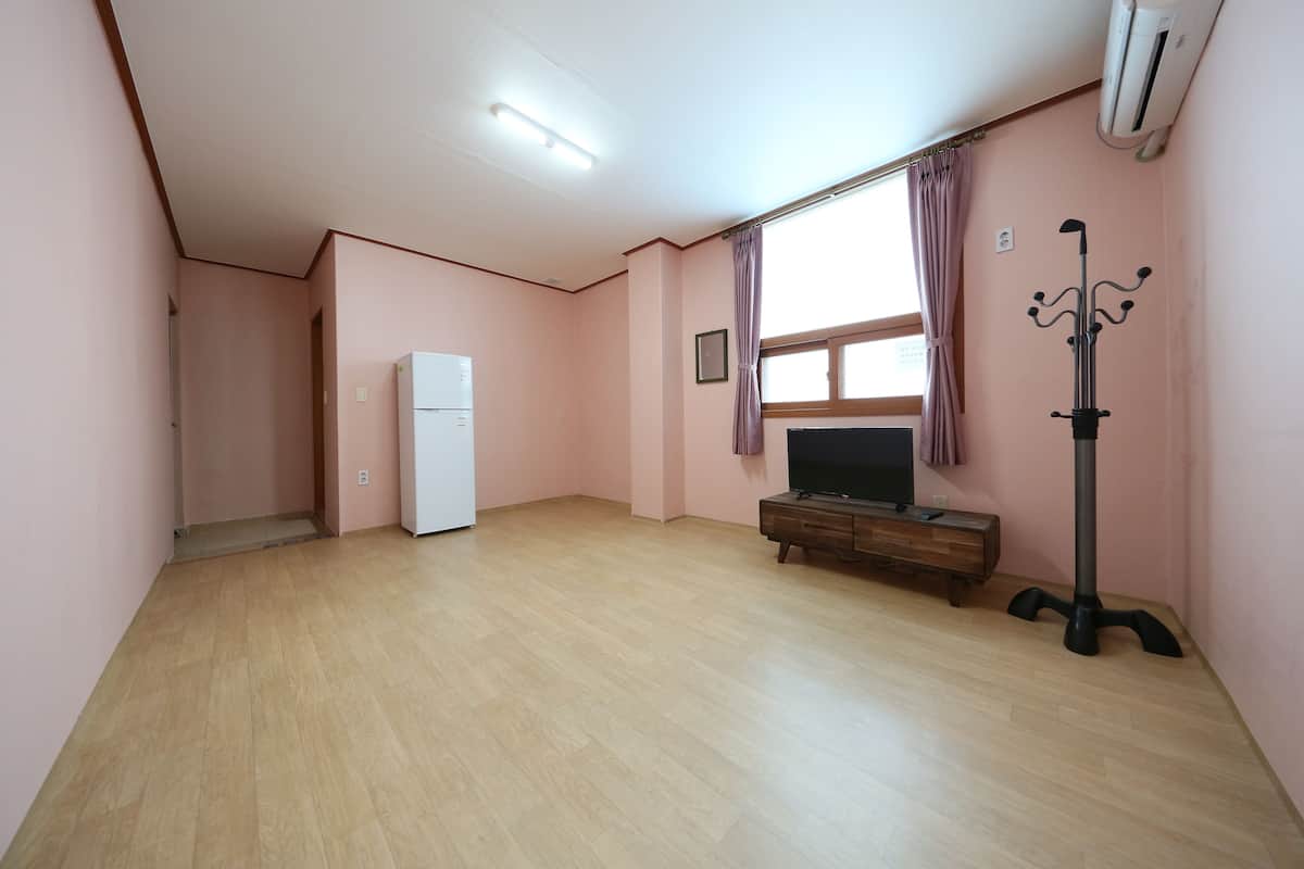 Una habitación amplia con suelo de madera, un refrigerador blanco, un televisor sobre un mueble de madera y un perchero.