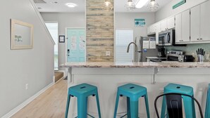 A modern kitchen with white cabinets, a granite countertop, and three turquoise bar stools. - Gem Beach House Steps to Beach&Pool+Opt Golf Cart (Miramar Beach)