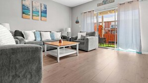 A modern living room with grey sofas, a wooden coffee table, and artwork on the wall. - Gem Beach House Steps to Beach&Pool+Opt Golf Cart (Miramar Beach)
