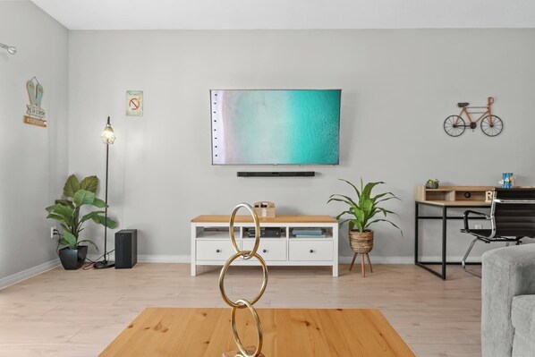 A modern living room with a flat-screen TV, white cabinets, a wooden coffee table, and two potted plants.