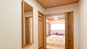 Ein schmaler Flur führt zu einem Schlafzimmer mit Bett und Fenster.