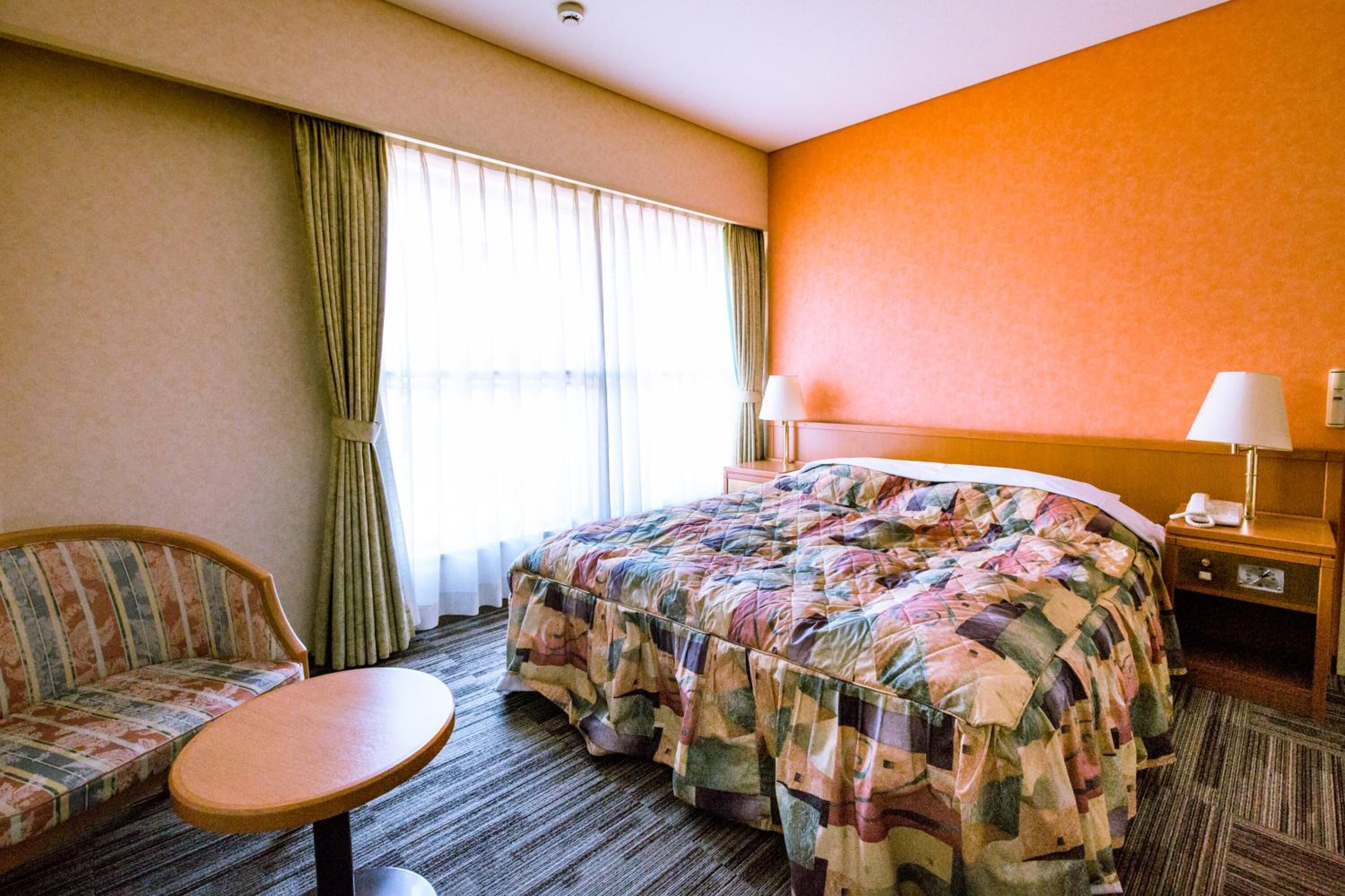 Ein Hotelzimmer mit Bett, Sofa, kleinem Tisch und Nachttisch mit Lampen.
