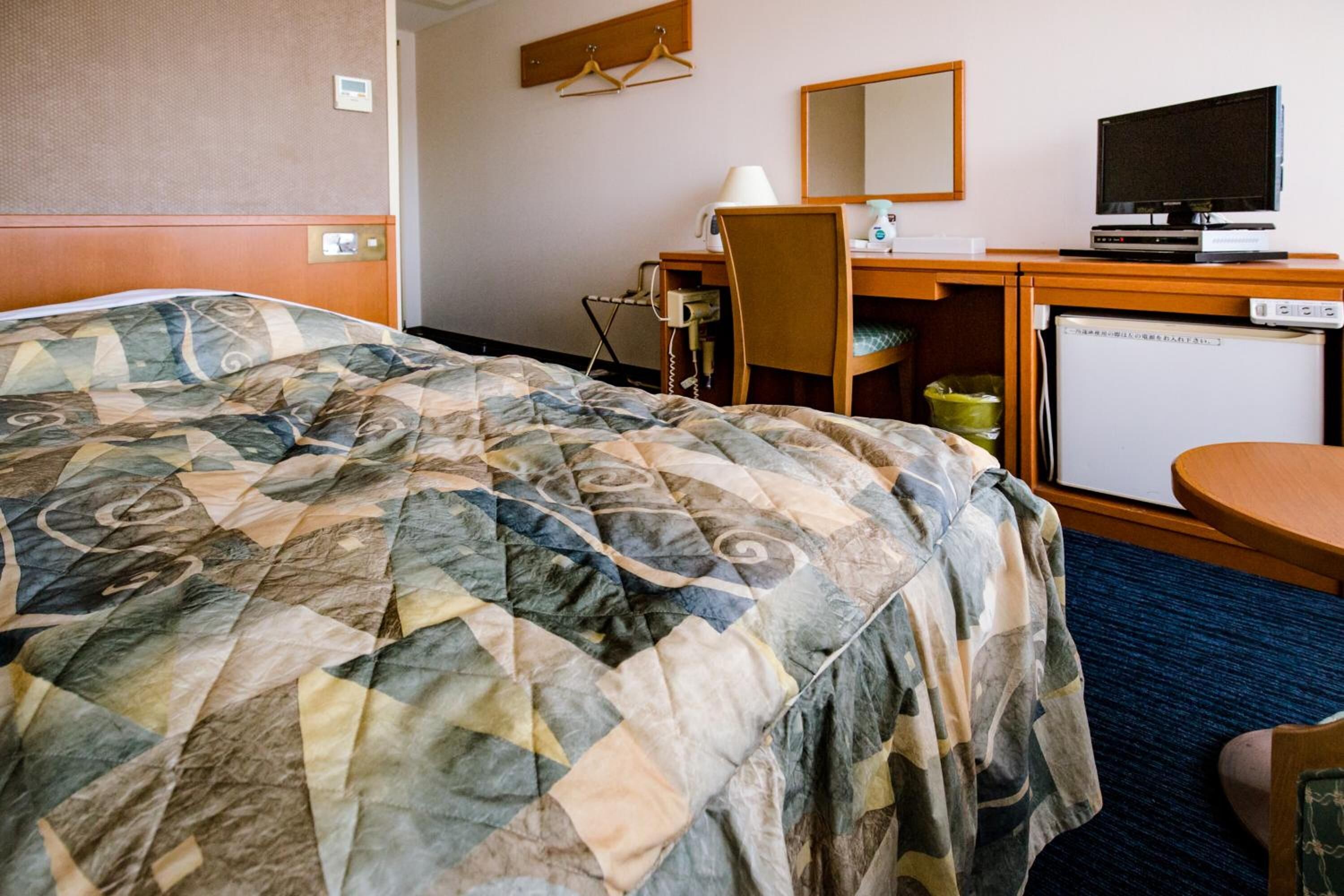 A hotel room with a bed, a desk with a computer, a television, and a small refrigerator.