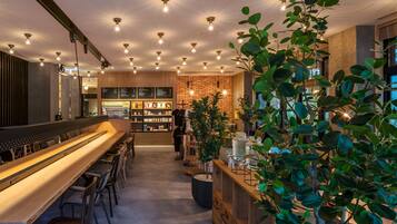 Un área de bar moderna con una barra alargada, asientos y una pared de ladrillo al fondo.