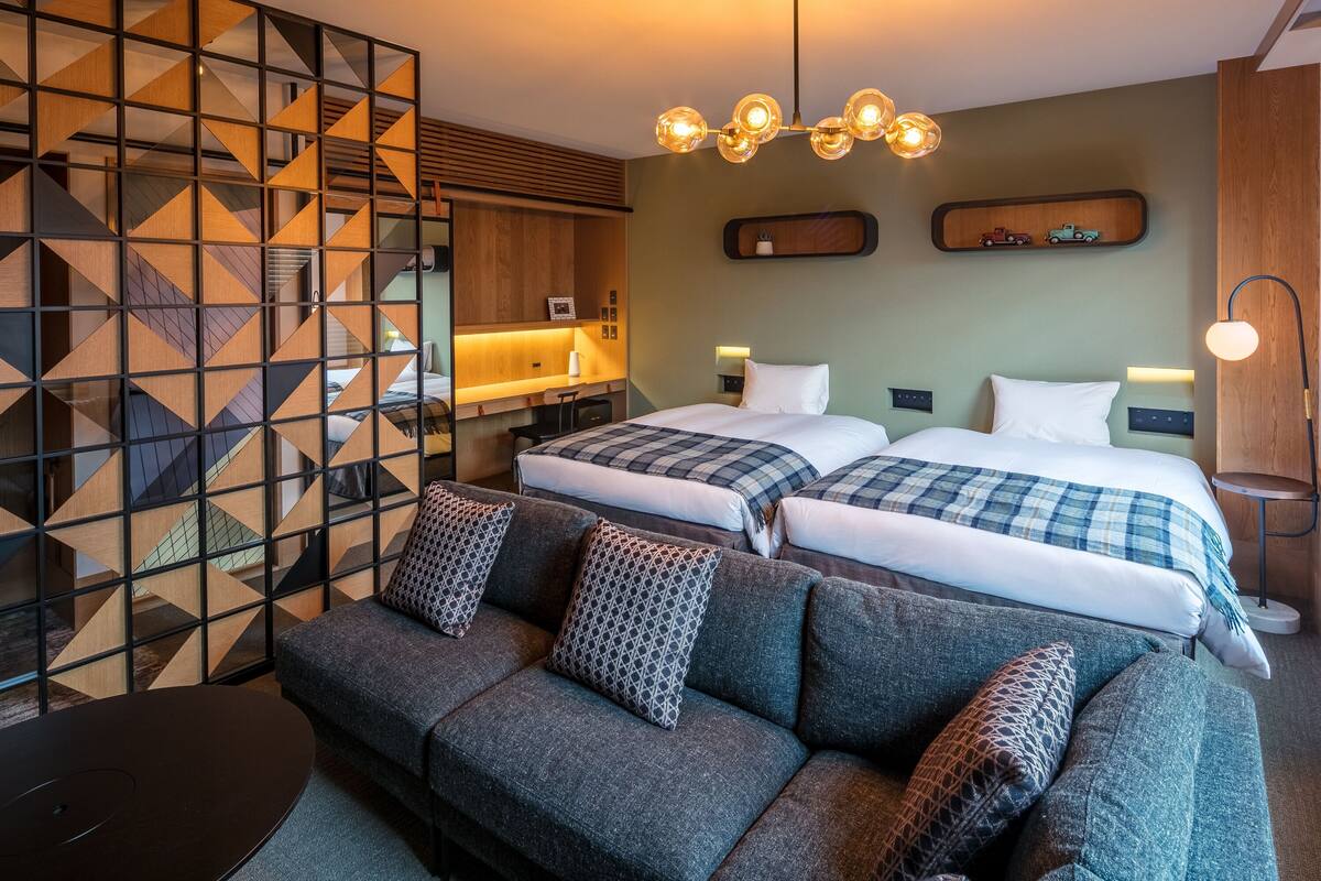 Habitación de hotel con dos camas, un sofá, un escritorio, kitchenette y un separador decorativo.
