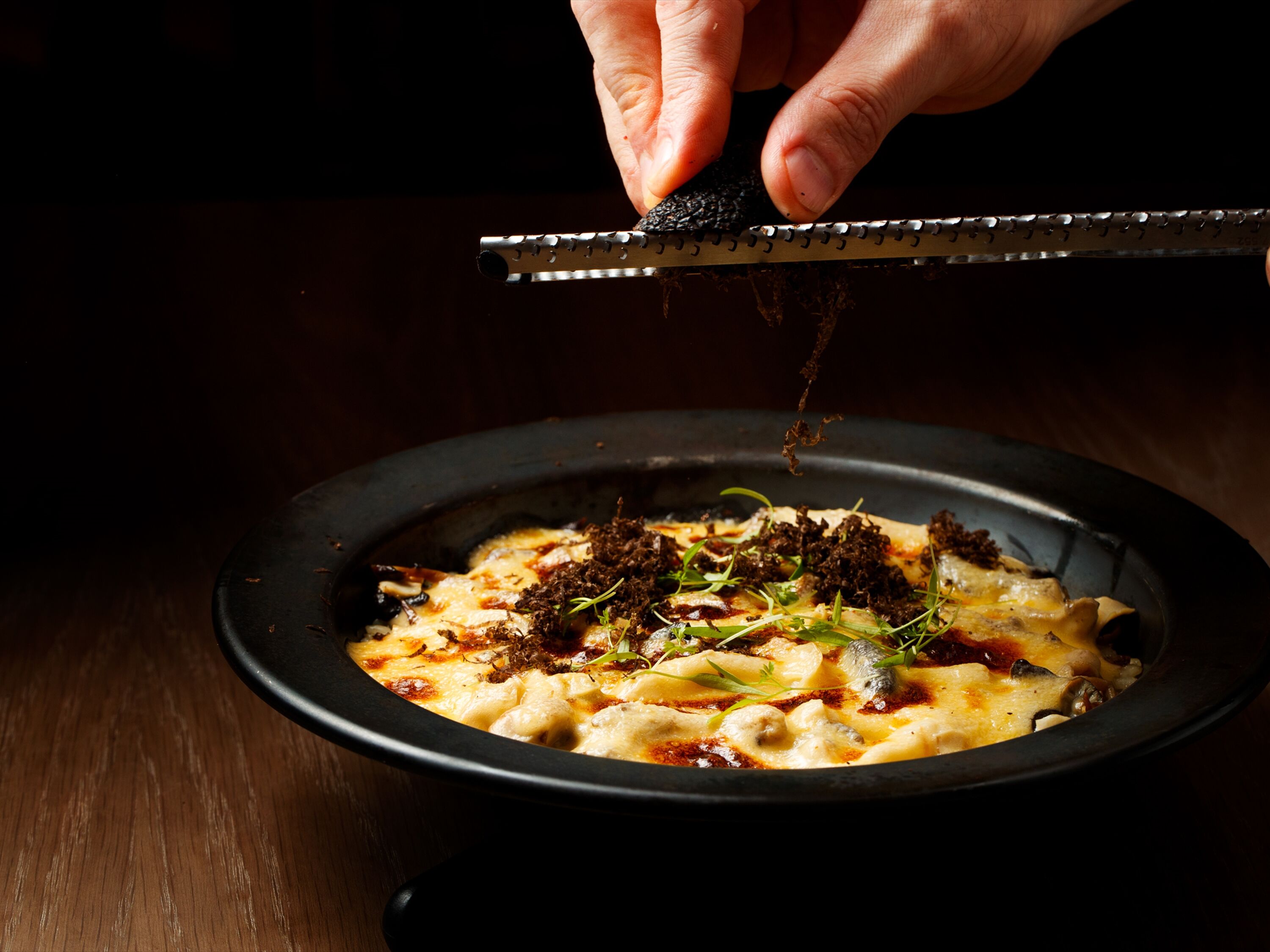 A dish with a black bowl, garnished with green herbs and topped with a dark topping.