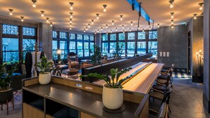 Un bar moderno con una barra larga, diversas opciones de asiento y grandes ventanales que ofrecen vistas al exterior.