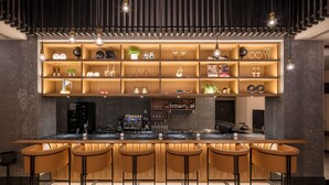 Zona de bar moderna con una barra alargada, varios taburetes y estanterías con distintos objetos.