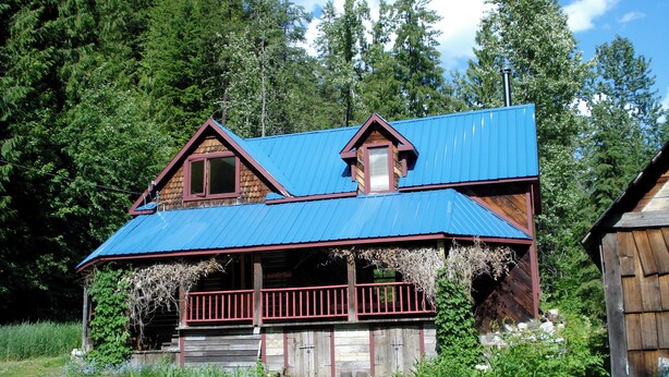 Une cabane rustique avec un toit en métal bleu, un revêtement extérieur en bois et une véranda dotée d’une balustrade rouge.
