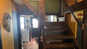 Un escalier en bois mène à un espace situé au deuxième étage, comprenant une cuisine et un coin repas.