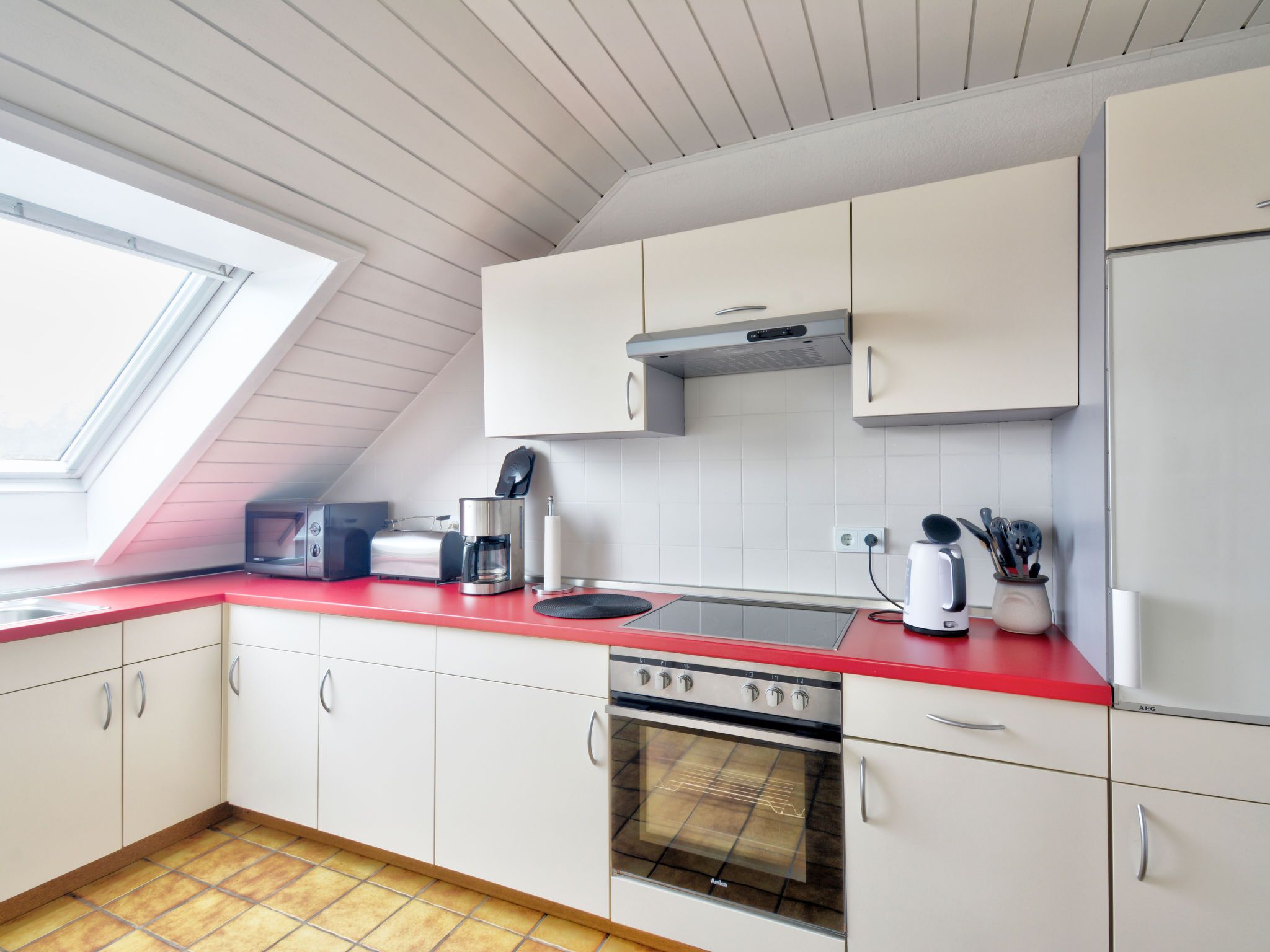 A modern kitchen with white cabinets, a red countertop, a built-in oven, and a coffee maker.