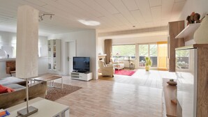 Una sala de estar amplia con un televisor de pantalla plana, un sofá, una mesa de centro y un comedor con una mesa y sillas.