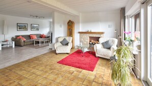 Un salón amplio con chimenea, dos sillones, un sofá y un tapete rojo.