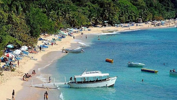 Una playa con un bote llamado "Glass Bottom Boat" anclado cerca de la orilla, rodeado de gente y sombrillas de playa.