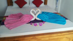 A bed with a wooden headboard, two red pillows, and a heart-shaped towel arrangement. - Tiny Holiday Resort (Dambulla)