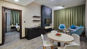 A modern hotel room with a dining area, a kitchenette, and a living space with blue chairs and a TV. - Express By TIME - Al Khan (Sharjah)