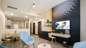 A modern hotel lobby with a TV, seating area, and a kitchen in the background. - Express By TIME - Al Khan (Sharjah)
