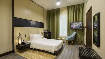 A hotel room with a bed, bedside table, lamp, TV, chair, and a small table with fruit.
