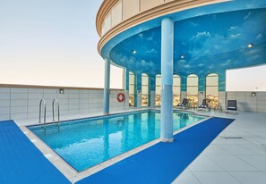 An indoor swimming pool with a blue-tiled floor, a lifebuoy, and a ceiling painted to resemble a sky with clouds. - Express By TIME - Al Khan (Sharjah)