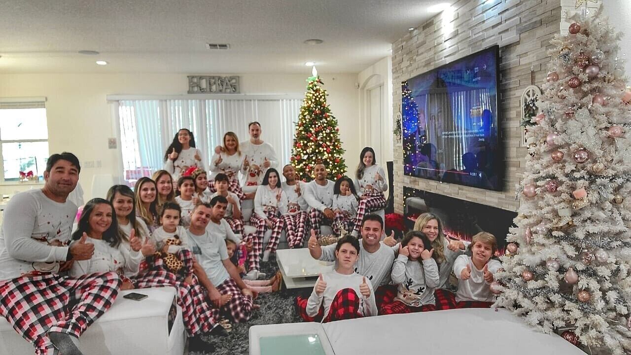 Een groep mensen in een woonkamer met een kerstboom, een televisie en een open haard.