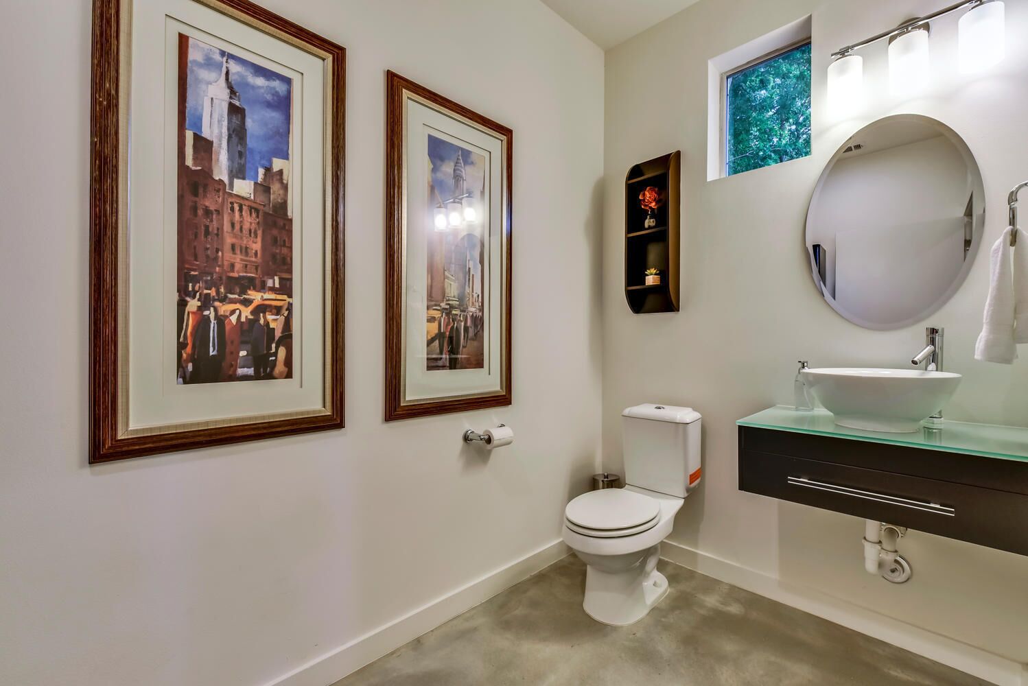 A bathroom with a toilet, a sink with a mirror, and two framed pictures on the wall.