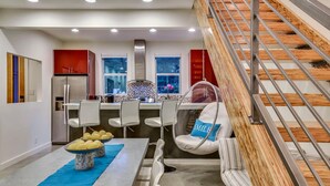 A modern kitchen with a dining area, a staircase, and a hanging chair. - Downtown Austin Luxury House with Hot Tub + Golf Green + Fire Pit +Patio Misters (Austin)