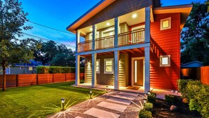 A two-story house with a balcony, a well-maintained lawn, and a gravel pathway leading to the entrance. - Downtown Austin Luxury House with Hot Tub + Golf Green + Fire Pit +Patio Misters (Austin)