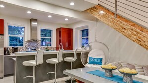 A modern kitchen with a bar area, a dining table with chairs, and a hanging chair with a 'SMILE' pillow. - Downtown Austin Luxury House with Hot Tub + Golf Green + Fire Pit +Patio Misters (Austin)