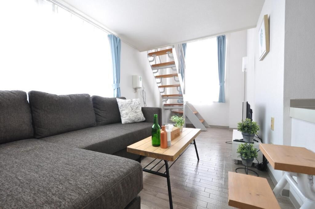 Una sala de estar moderna con un sofá gris, una mesa de centro de madera y una escalera que sube a un nivel superior.