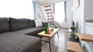 Una sala de estar moderna con un sofá gris, una mesa de centro de madera y una escalera que sube a un nivel superior.