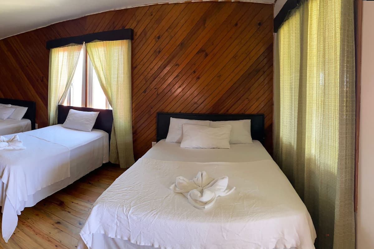 A hotel room with three single beds, each with a white bedspread and pillows, and a wooden floor.