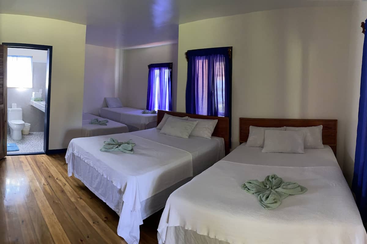 A hotel room with two single beds, a wooden floor, a small table, and a bathroom visible through an open door.
