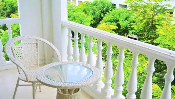 Ein weißer Korbstuhl und ein Tisch auf einem Balkon mit weißen Geländern, mit Blick auf üppiges Grün.