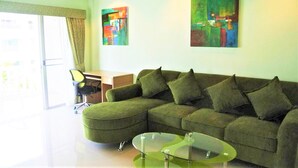 Ein modernes Wohnzimmer mit einem grünen Ecksofa, zwei Glastischen und abstrakten Bildern an den Wänden.