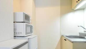 Eine kleine Küche mit weißen Geräten, darunter eine Mikrowelle und ein Kühlschrank, sowie hellem Küchenschrank