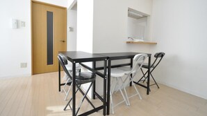 A modern, minimalist room with a wooden door, a black table with four chairs, and a small shelf with a mirror above it. - IK Minami6Jo Residence 301 (Sapporo)