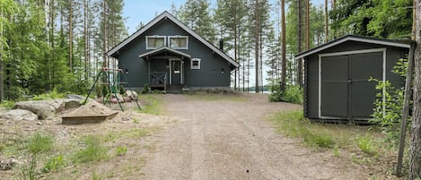 Une cabane avec une allée en gravier, entourée de grands arbres.