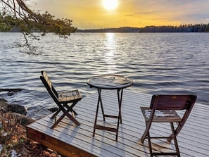A wooden deck with two chairs and a small round table overlooking a calm lake at sunset. - Vacation home Kantri by Interhome (Ruokolahti)