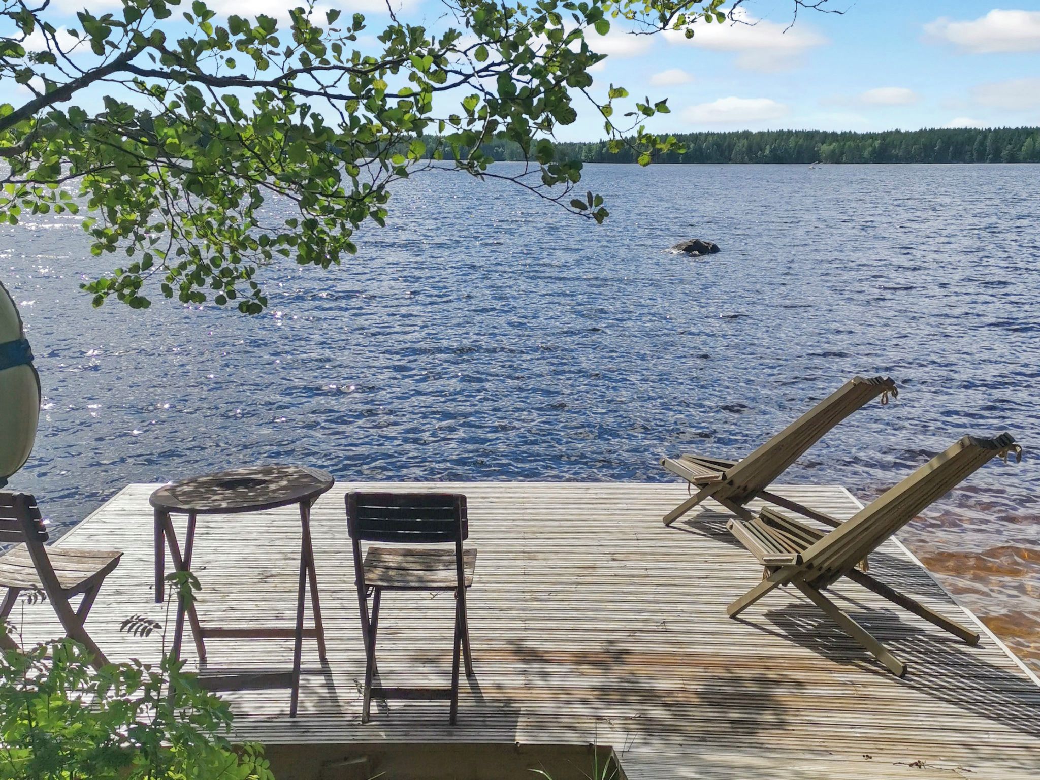 A wooden deck with lounge chairs and a table overlooking a lake.