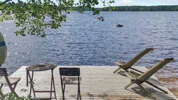 A wooden deck with lounge chairs and a table overlooking a lake.